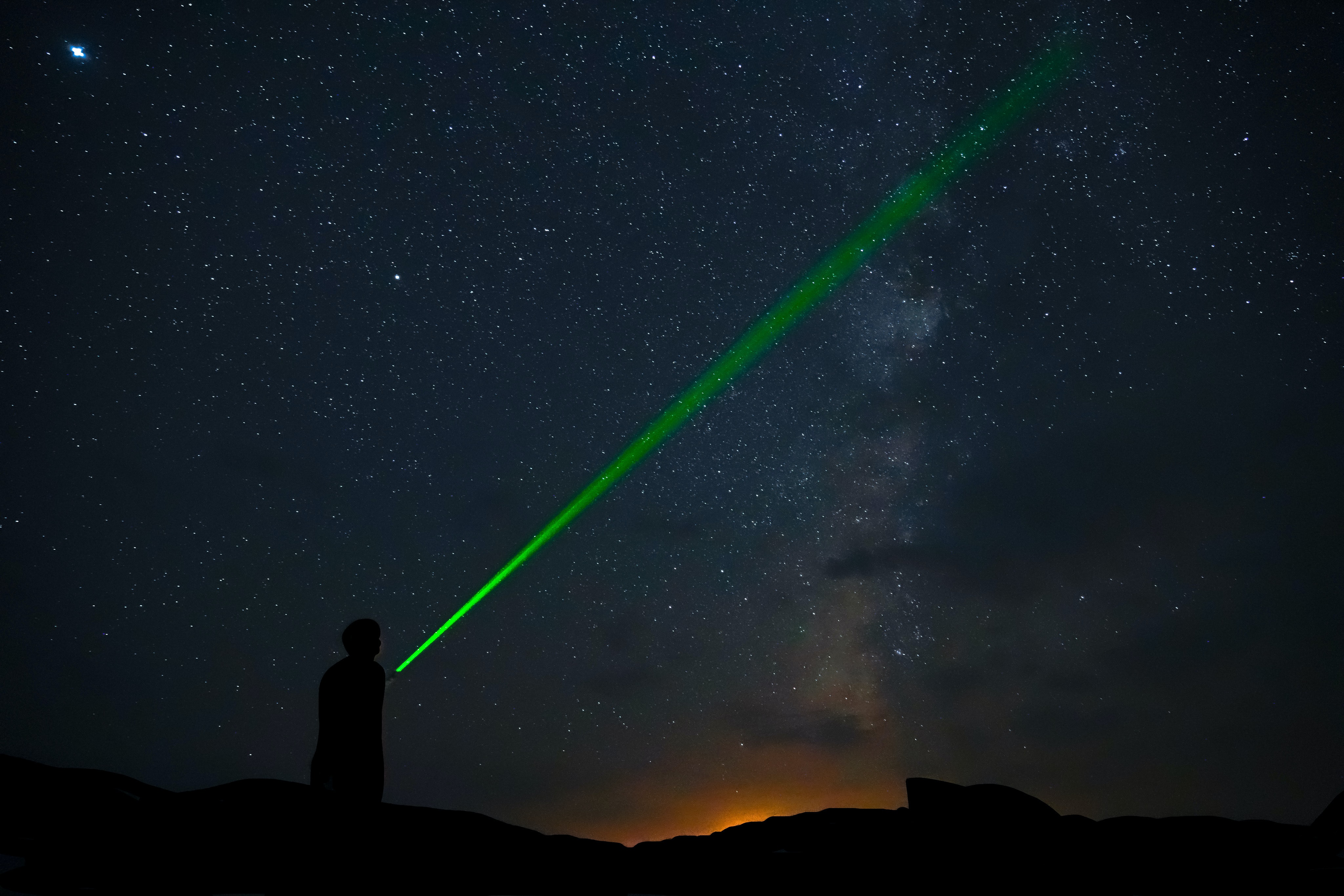 A man pointing a green laser at the night sky